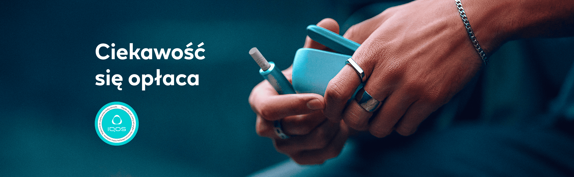 Urządzenia IQOS w kolorze niebieskim oraz napis 'Ciekawość się opłaca' na granatowym, rozmytym tle