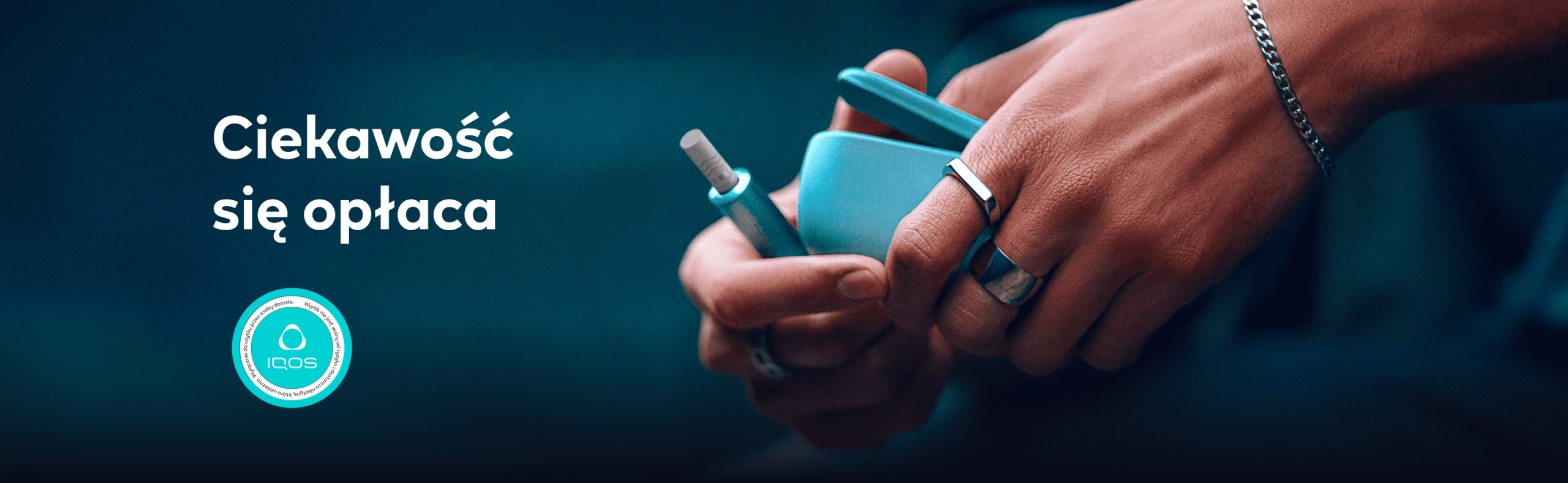 Urządzenie IQOS w kolorze niebieskim oraz napis 'Ciekawość się opłaca' na granatowym, rozmytym tle
